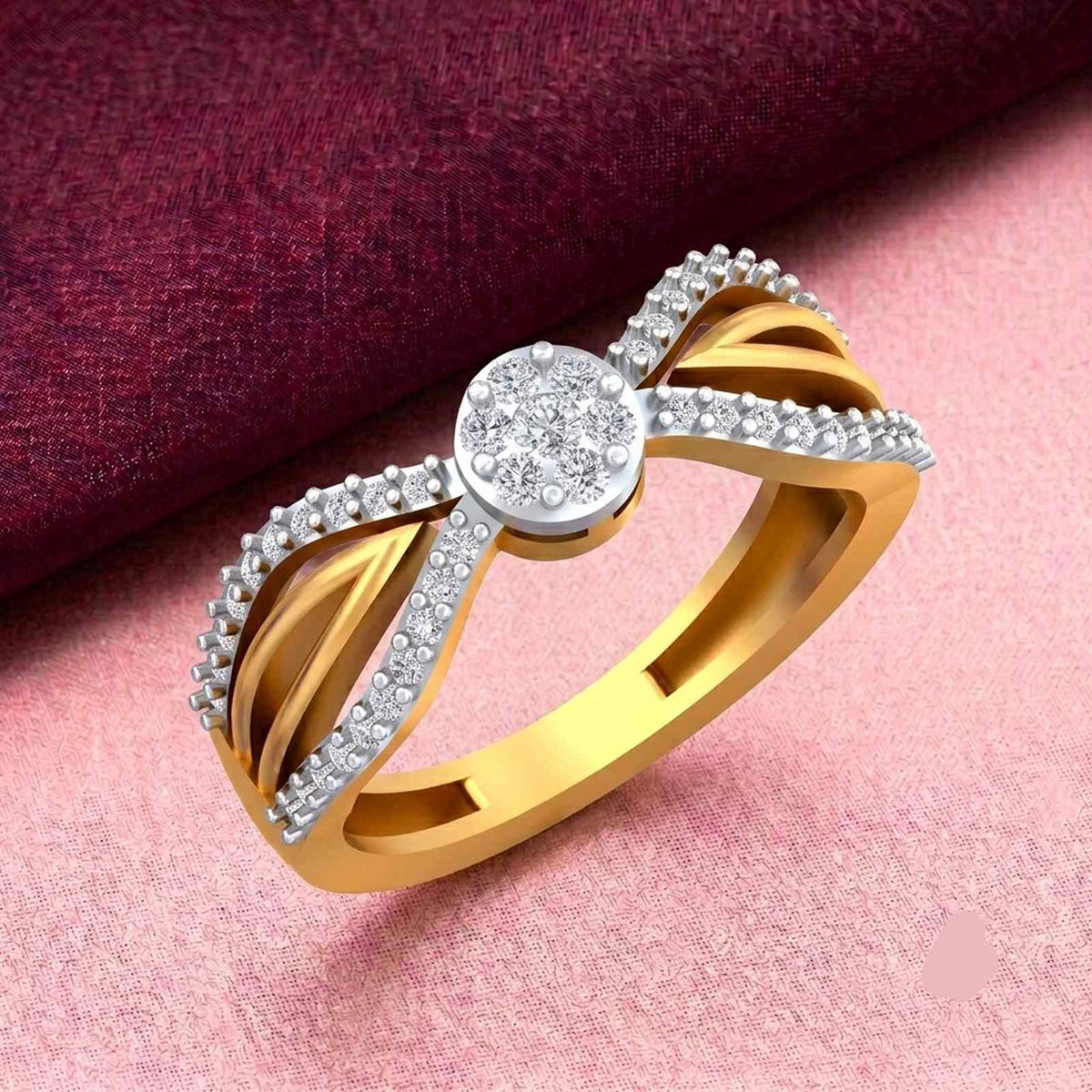 A gold and diamond ring, featuring a central round cluster, displayed on a pink textured surface with a dark burgundy fabric background.