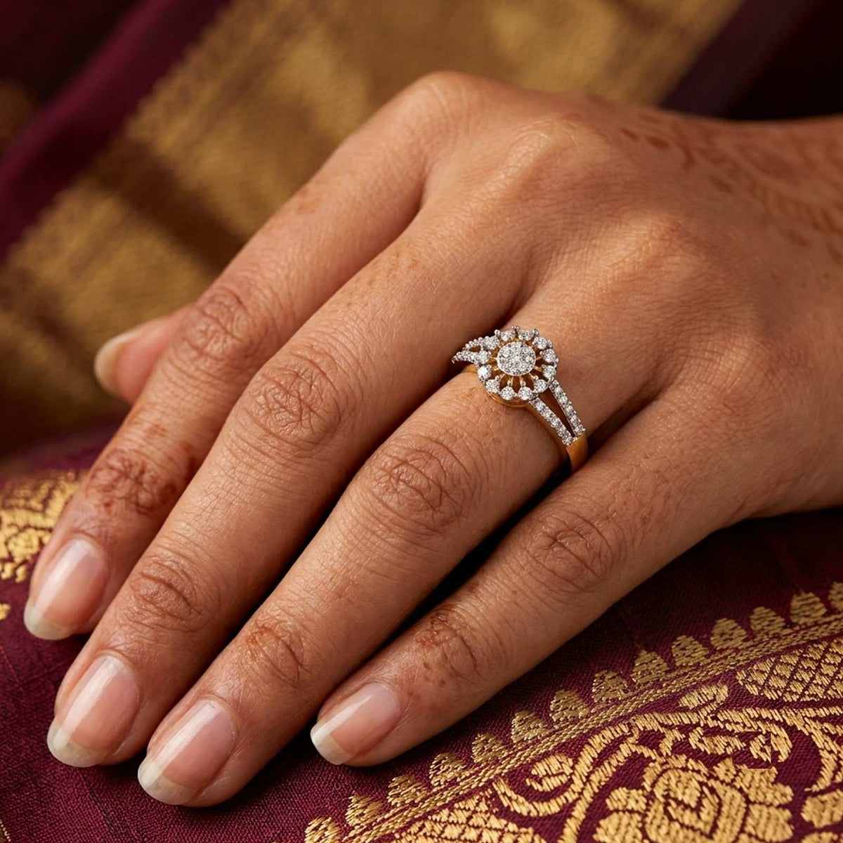 A close-up of a hand wearing a diamond ring with a gold band, resting on a deep maroon and gold patterned fabric.