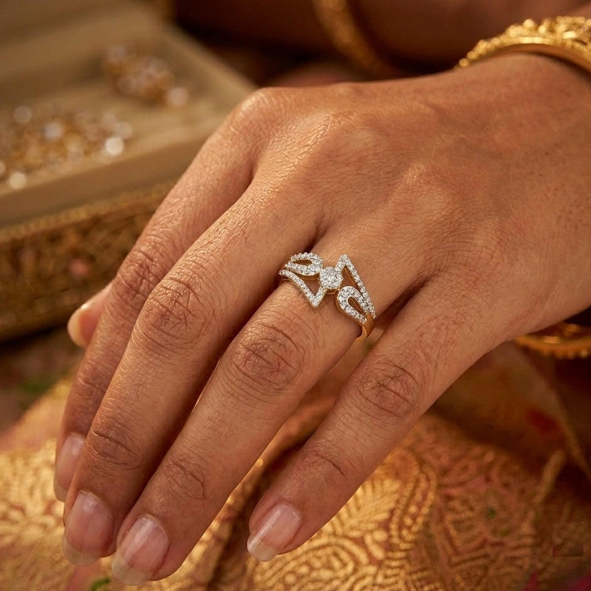 A close-up of a hand wearing a diamond ring, with gold-toned jewelry and a patterned fabric in the background.