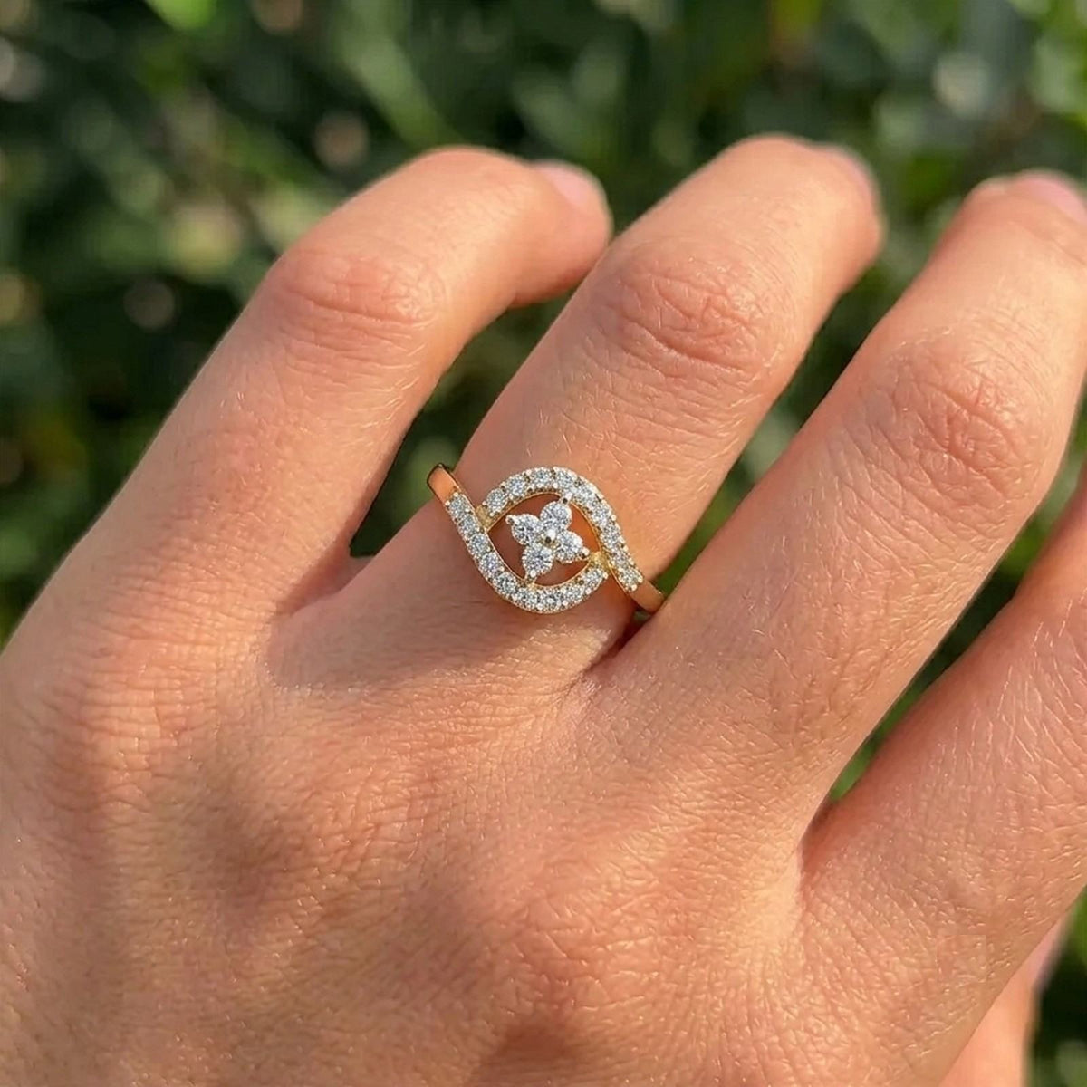 A close-up of a hand wearing a gold and diamond ring on a blurred green foliage in the background.