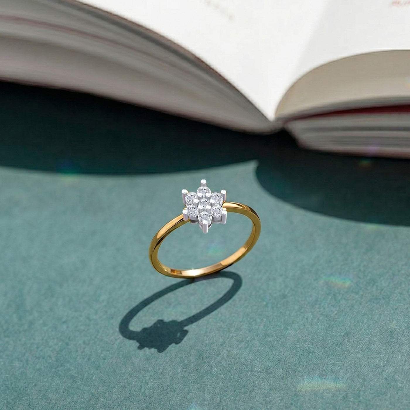 A gold and diamond ring with a floral cluster set, resting on a textured teal surface.