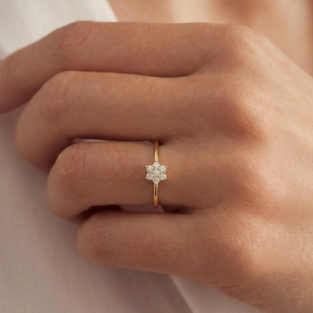 Close-up of a hand wearing a gold ring with a diamond on a neutral background