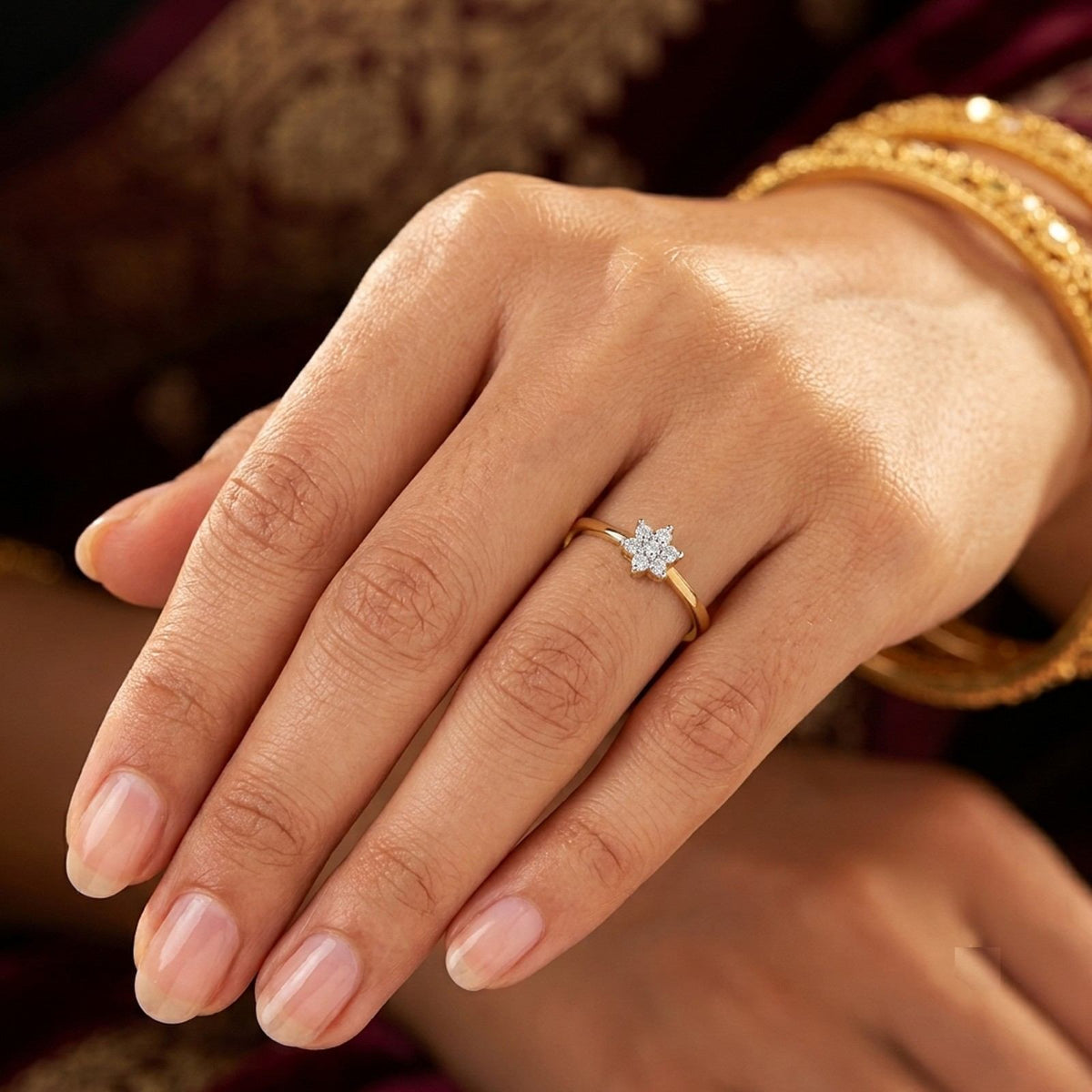 Close-up of a hand wearing a gold ring with a diamond on a maroon saree.