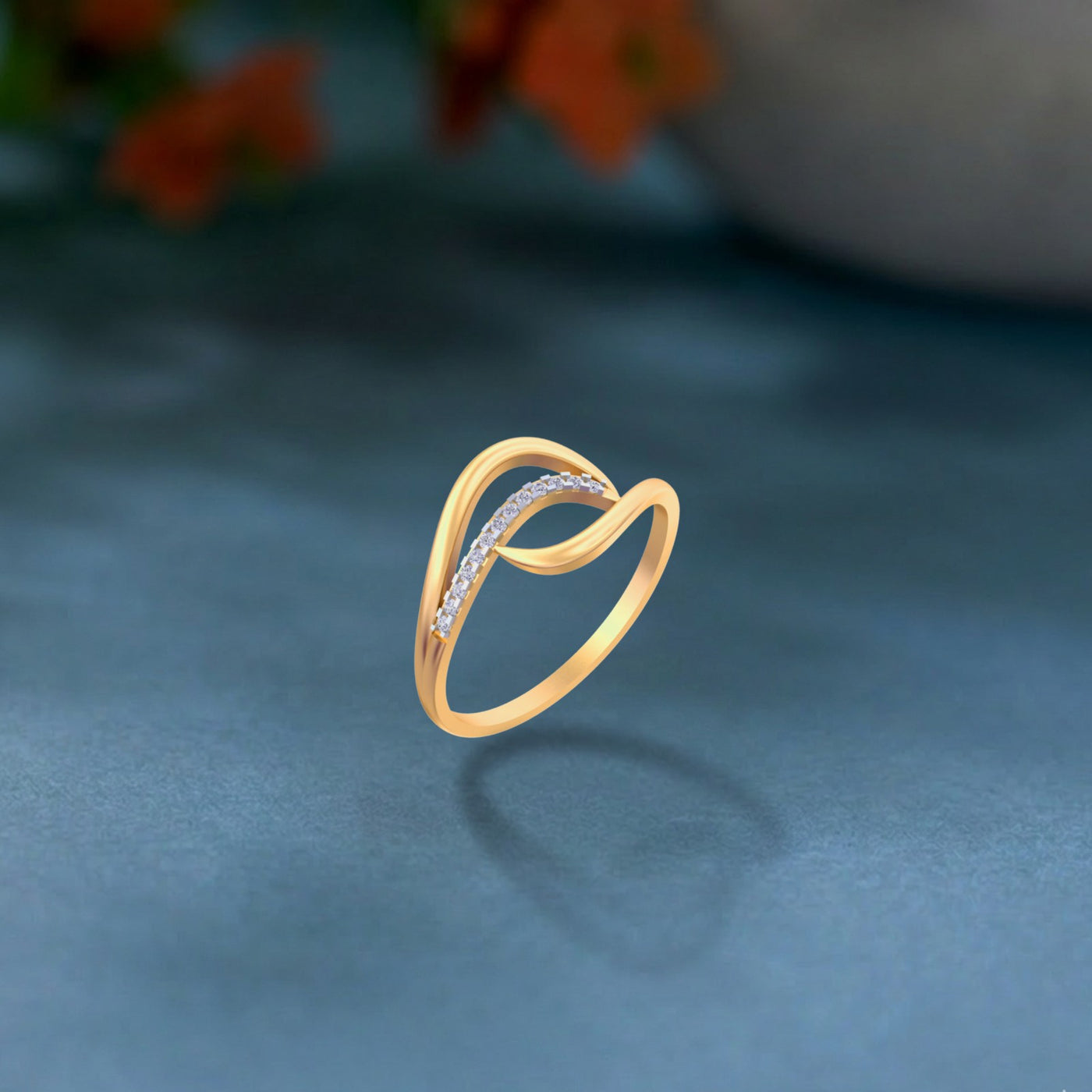 A gold and diamond design on a soft blue surface with blurred orange flowers in the background.