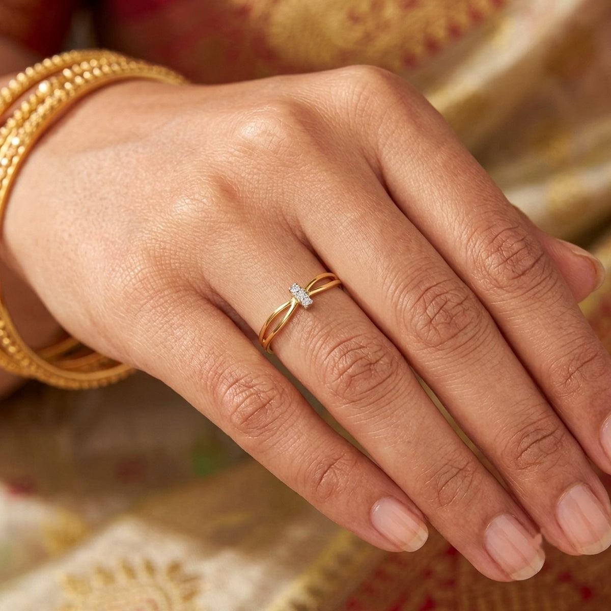 A close-up of a hand wearing a delicate gold ring, patterned fabric background.