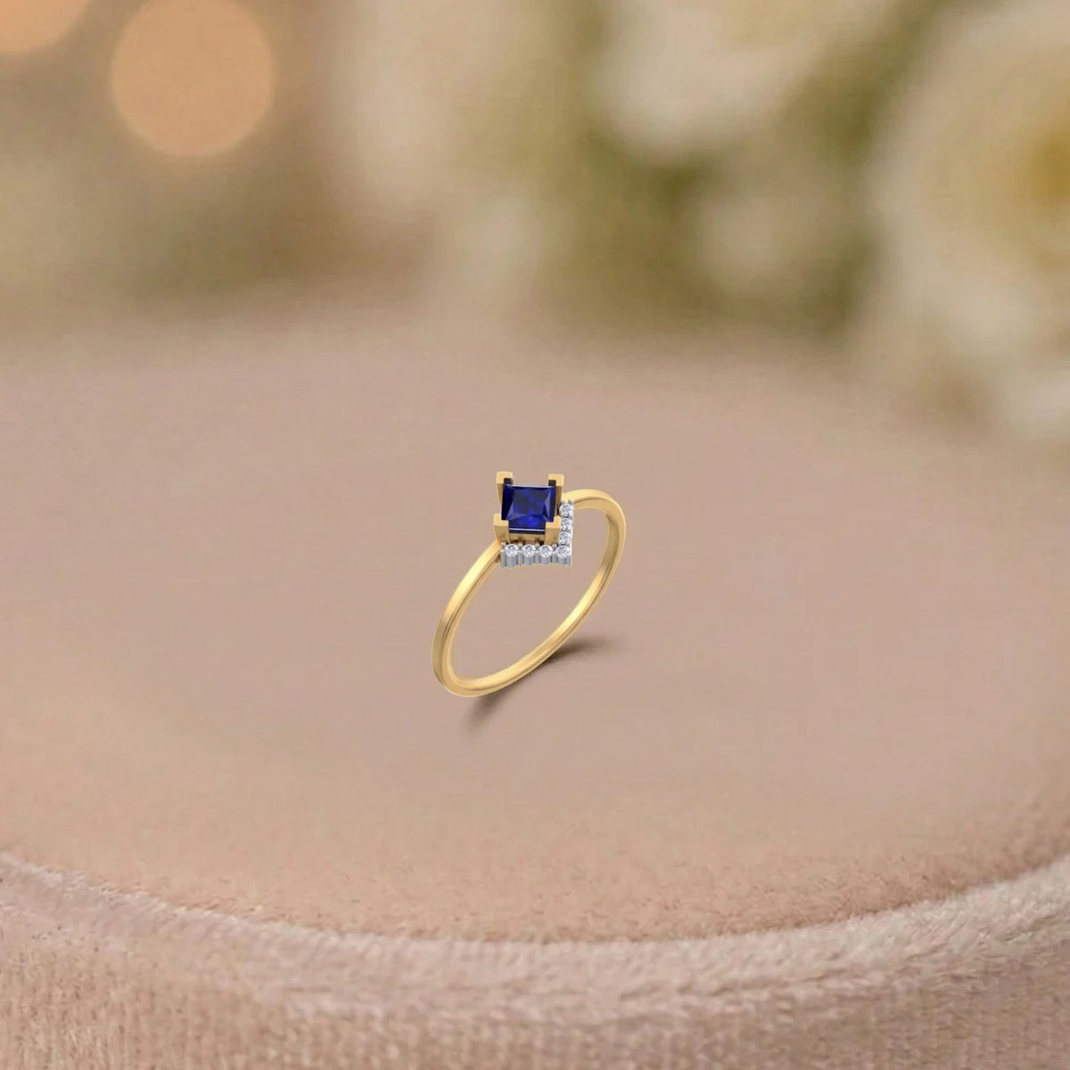 Gold and diamond with square-shaped sapphire gemstone setting on a beige surface.
