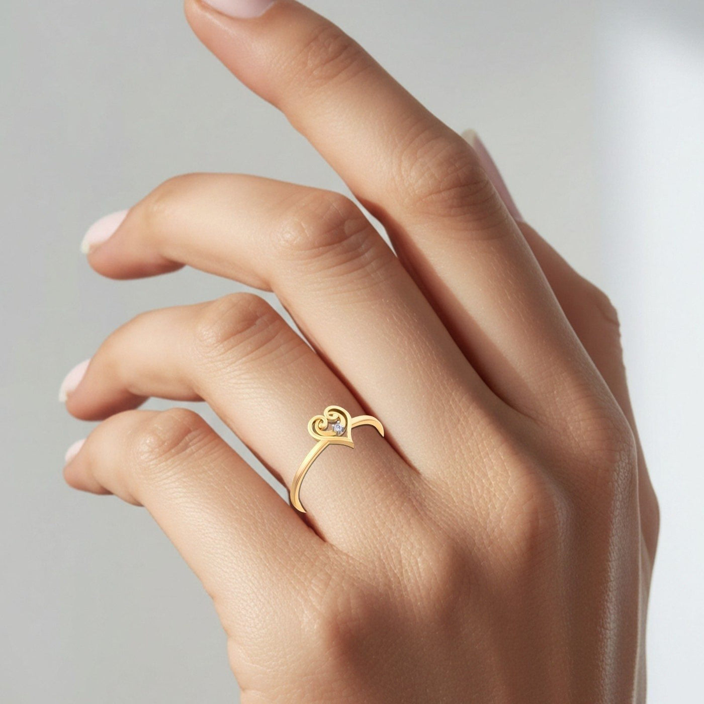 Gold ring with a heart design on a hand against a neutral background