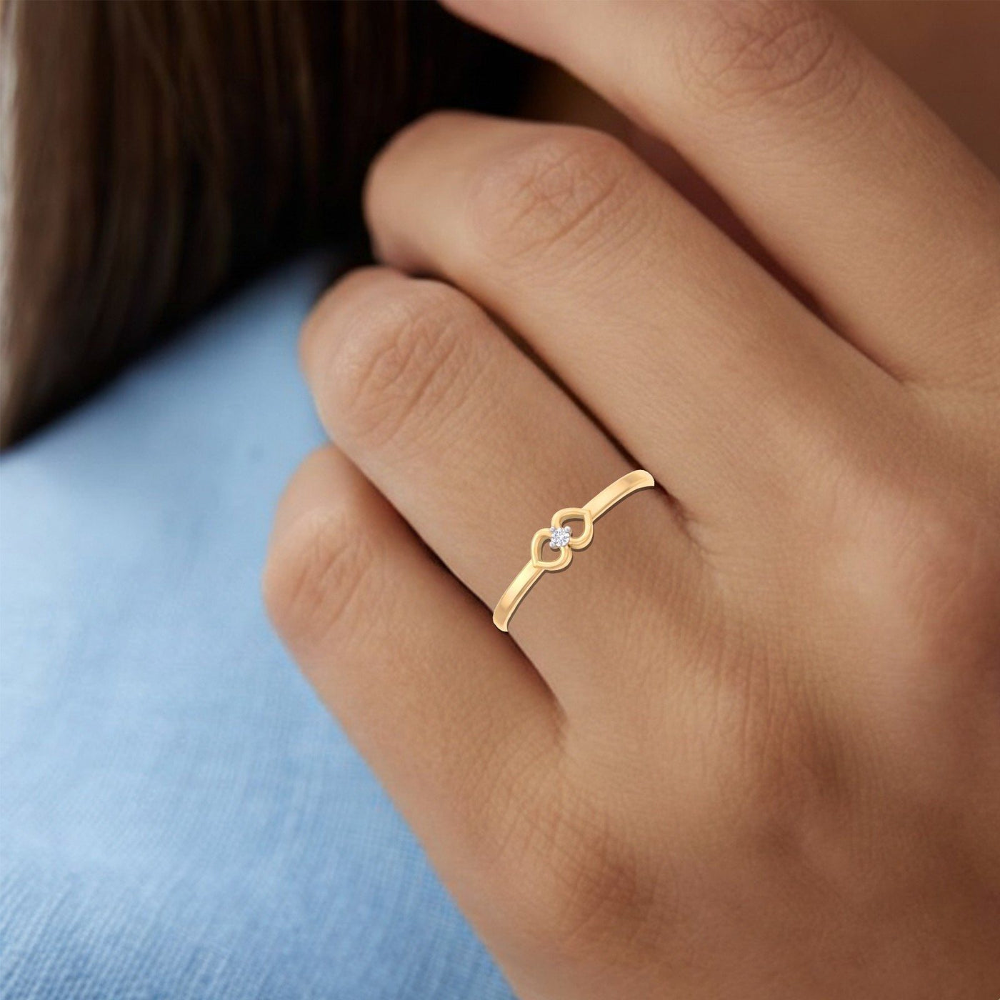 Gold ring with a small stone on a person's finger against a blue fabric background