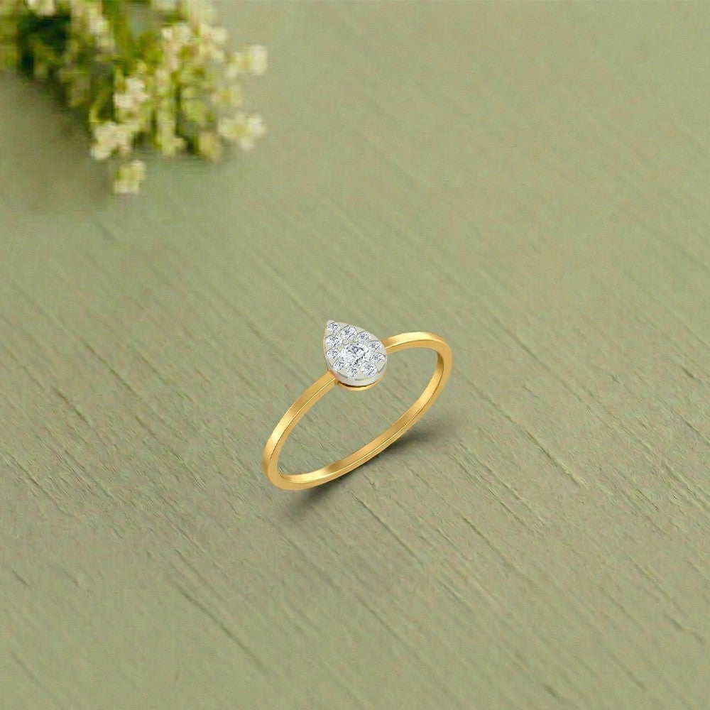 Gold and diamond ring with a teardrop-shaped center cluster on a green surface.