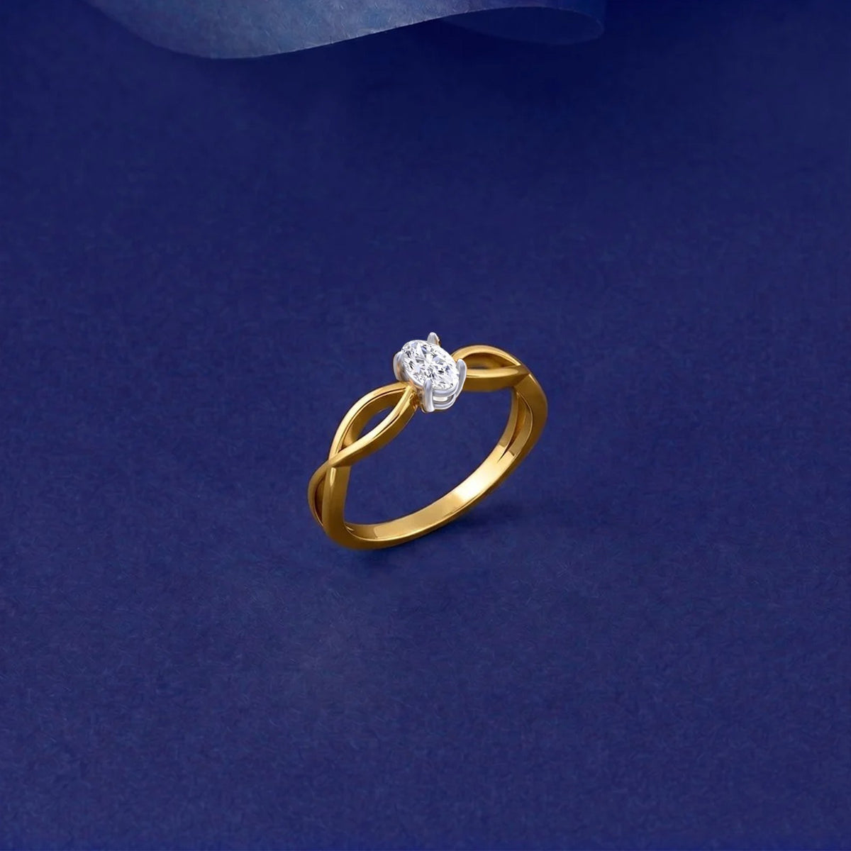 A gold and diamond ring with a twisted band design, displayed on a dark blue textured background.