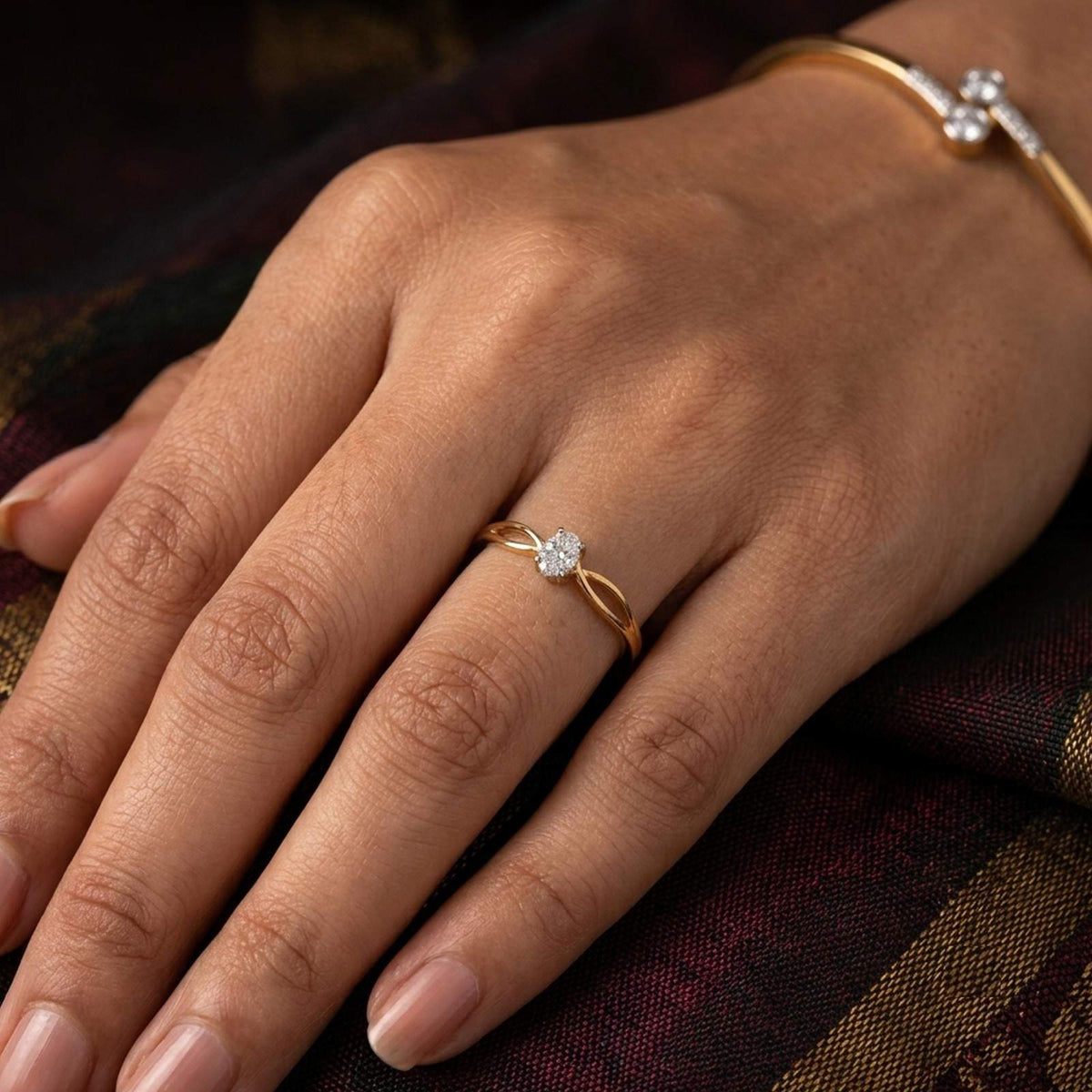 A close-up of a hand wearing a delicate gold and diamond ring, resting on a dark patterned fabric background.