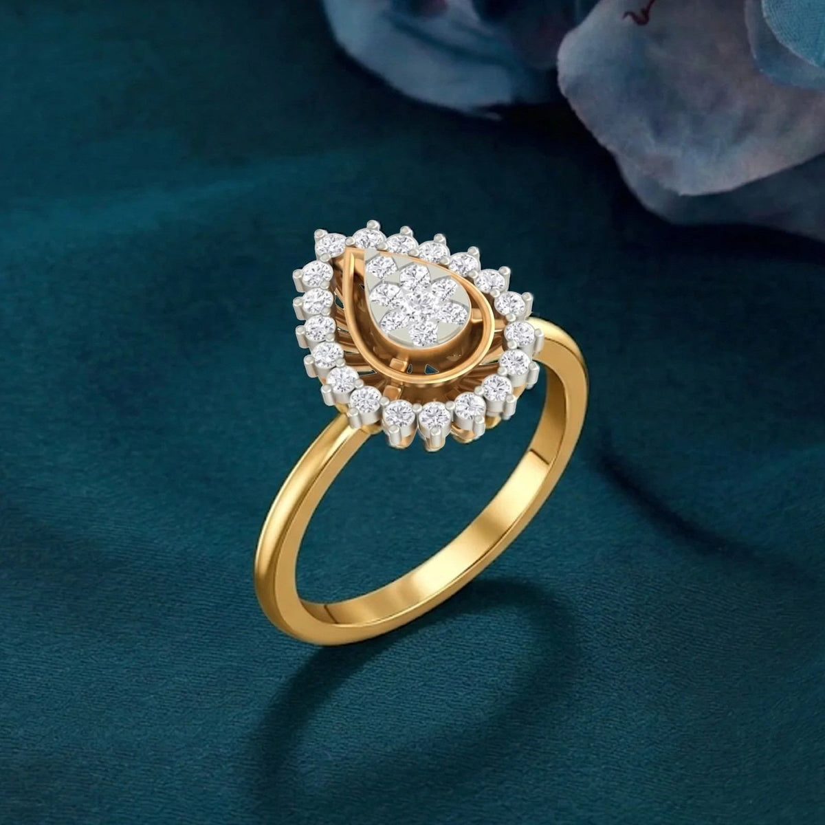 A gold and diamond ring with a teardrop-shaped cluster, set on a teal surface.