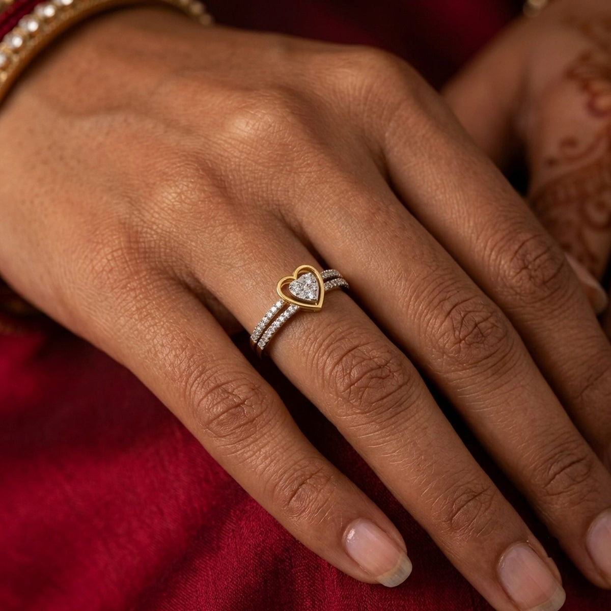 Gold heart-shaped ring on a person's finger with a red saree background.