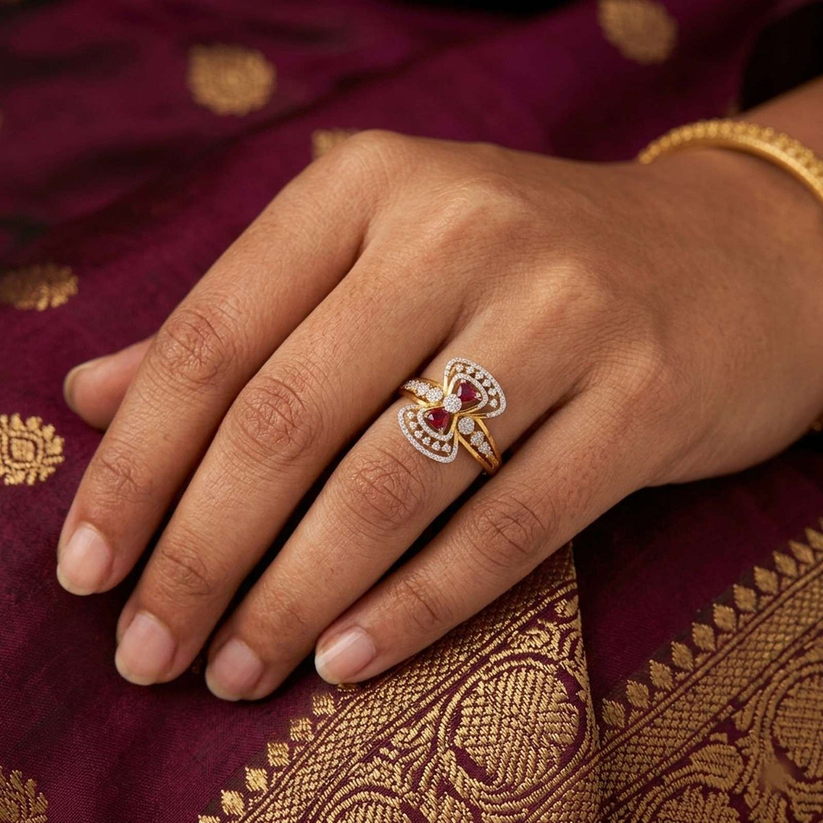 Gold ring with ruby gemstones and diamond accents on a person's finger.