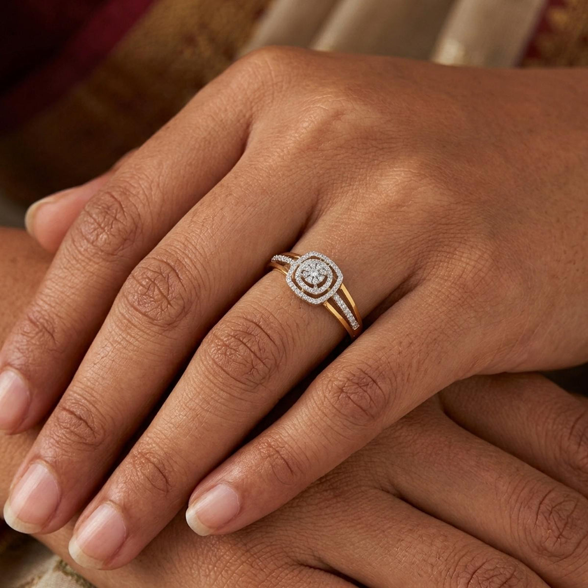A close-up of a hand wearing a gold ring with a diamond-set oval center and a halo of small diamonds, resting on another hand.