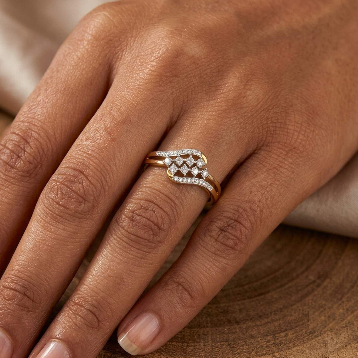 Gold ring with diamonds on a person's finger against a wooden background