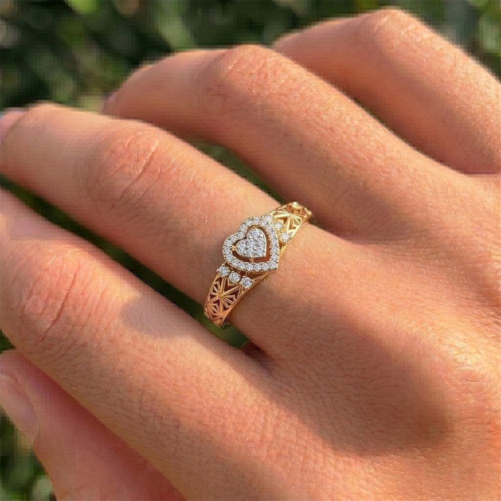 Gold ring with heart-shaped diamond design on a hand against a blurred green background