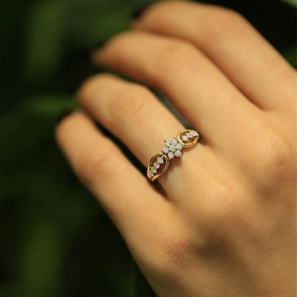 A gold and diamond ring, worn on a person's finger against a dark green blurred background.