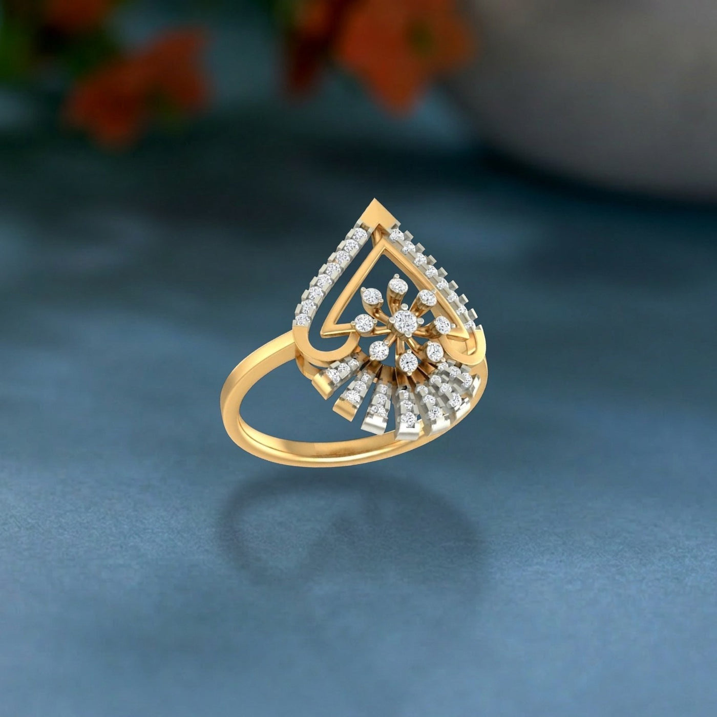 A gold ring featuring a teardrop-shaped pavé setting with a central floral cluster on a soft blue surface.