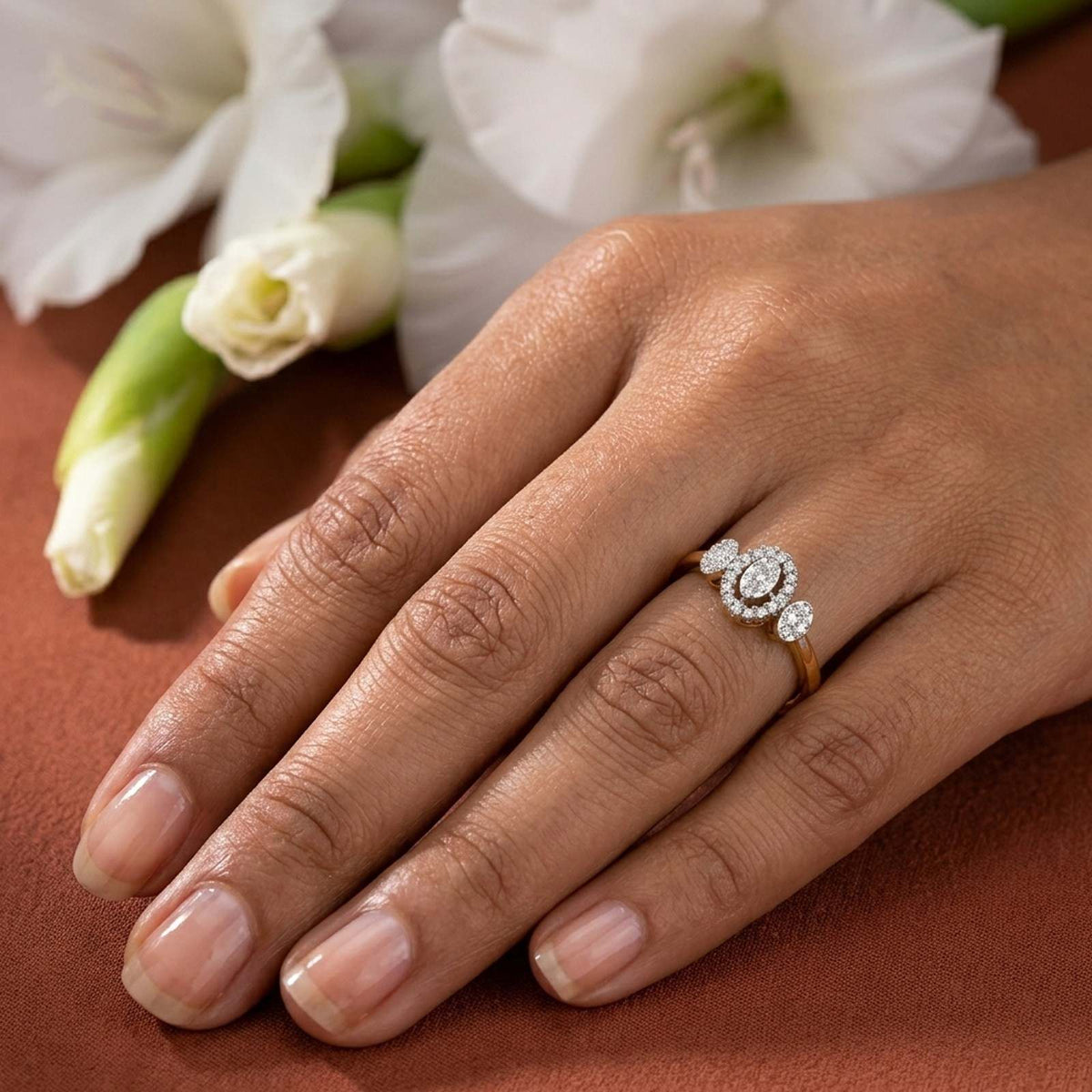 A close-up of a hand wearing a gold ring with a circular cluster, resting on a warm brown surface.