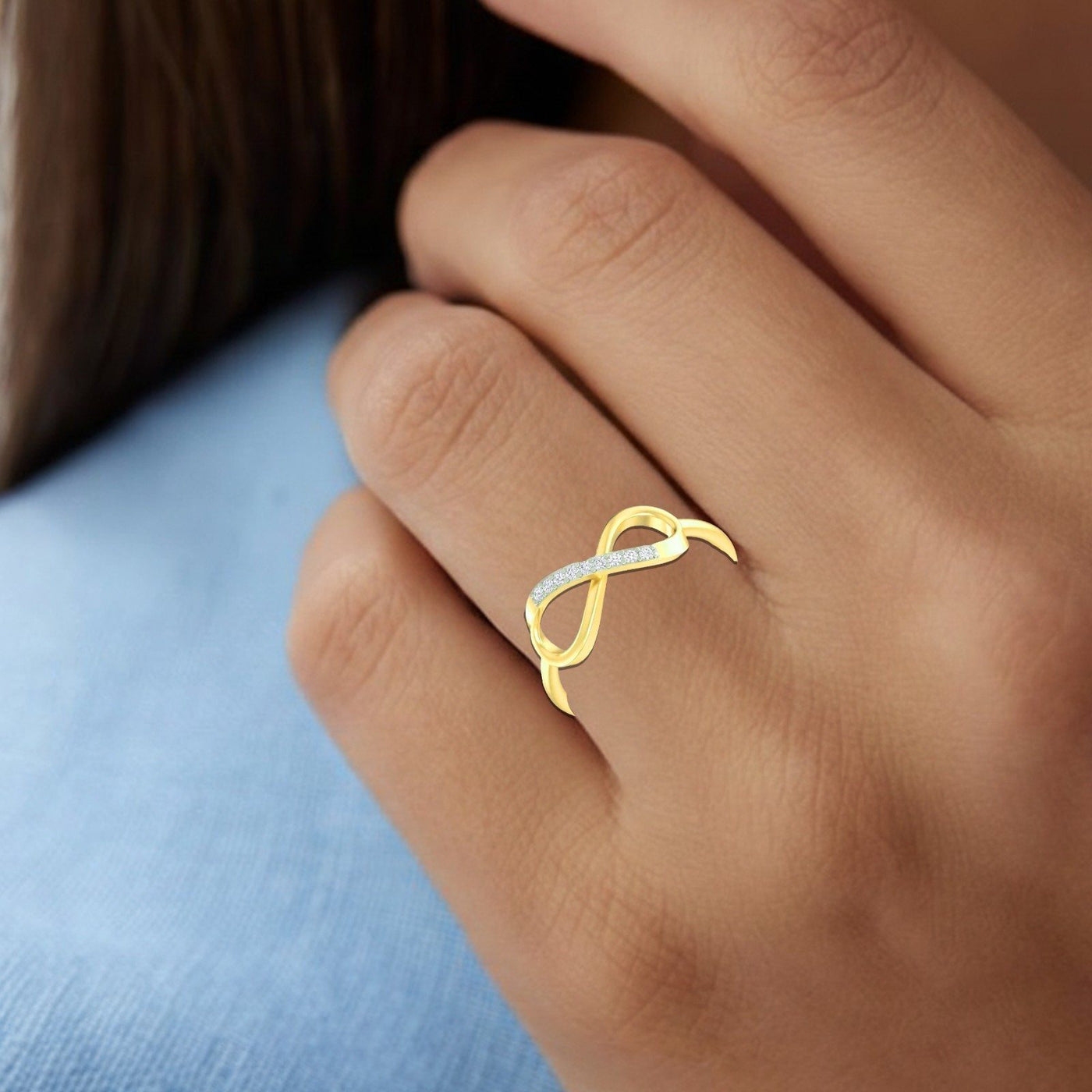 Gold ring with diamonds on a person's finger against a blue fabric background