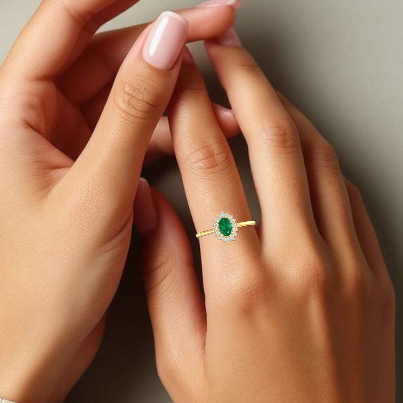 Close-up of a hand wearing a gold ring with a emerald gemstone on a neutral background
