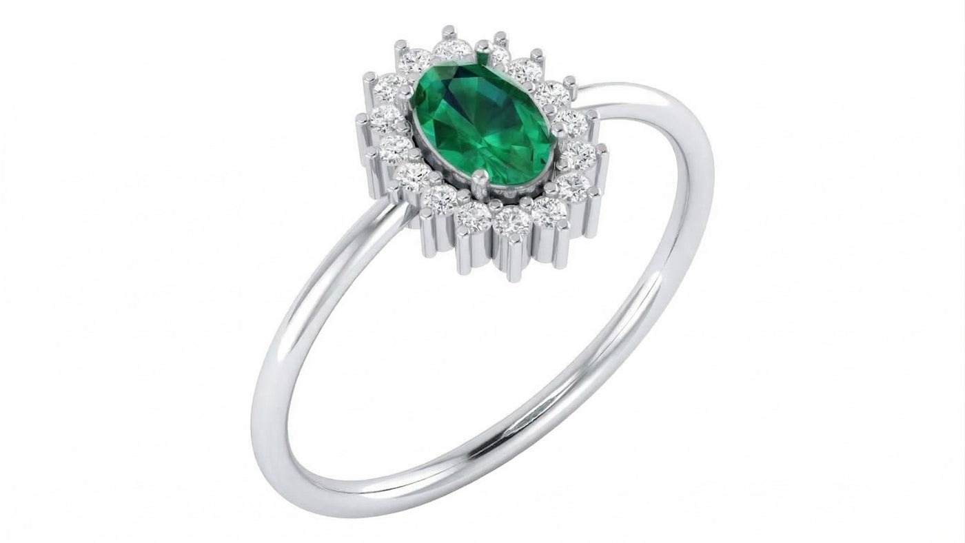 A white gold ring featuring a emerald gemstone center stone surrounded by a halo of small clear stones, set on a plain white background.