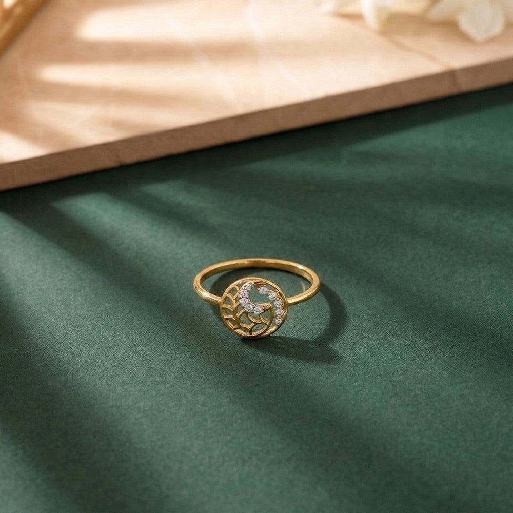 A gold ring featuring a circular design, resting on a dark green textured surface with soft shadows.