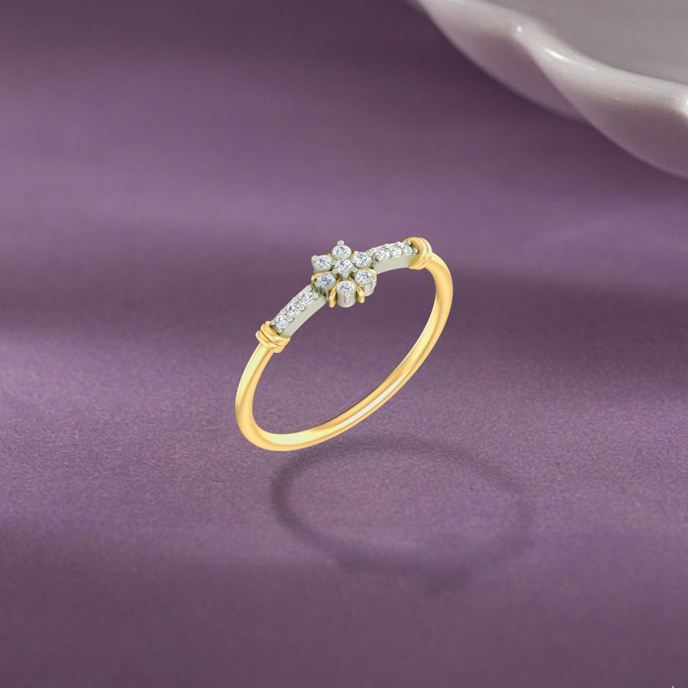 A delicate gold ring with a small floral cluster, displayed on a textured purple surface.