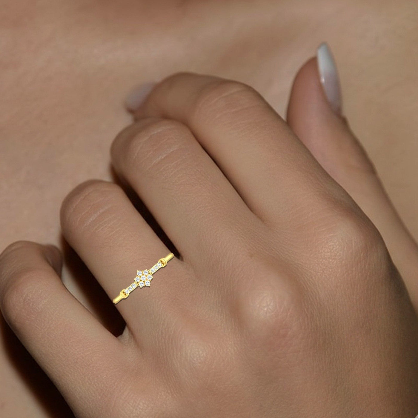 A delicate gold ring with a small white floral center, worn on a woman's ring finger.