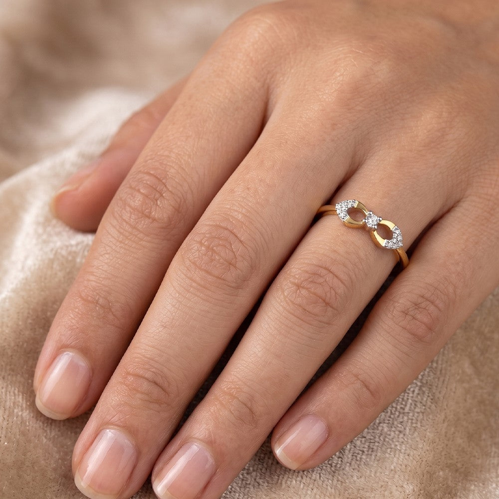 A close-up of a hand wearing a gold and diamond infinity ring, resting on a soft beige fabric background.