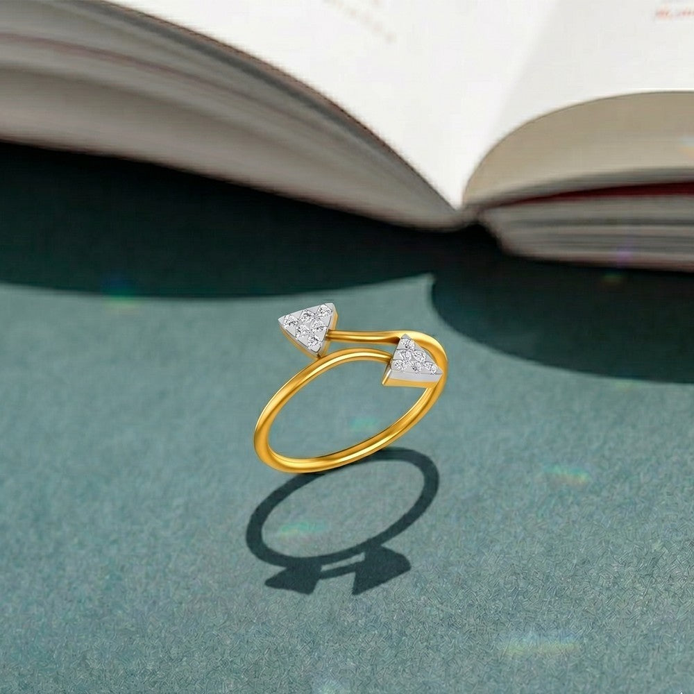 Gold ring with triangle-shaped diamonds on a green surface with an open book in the background