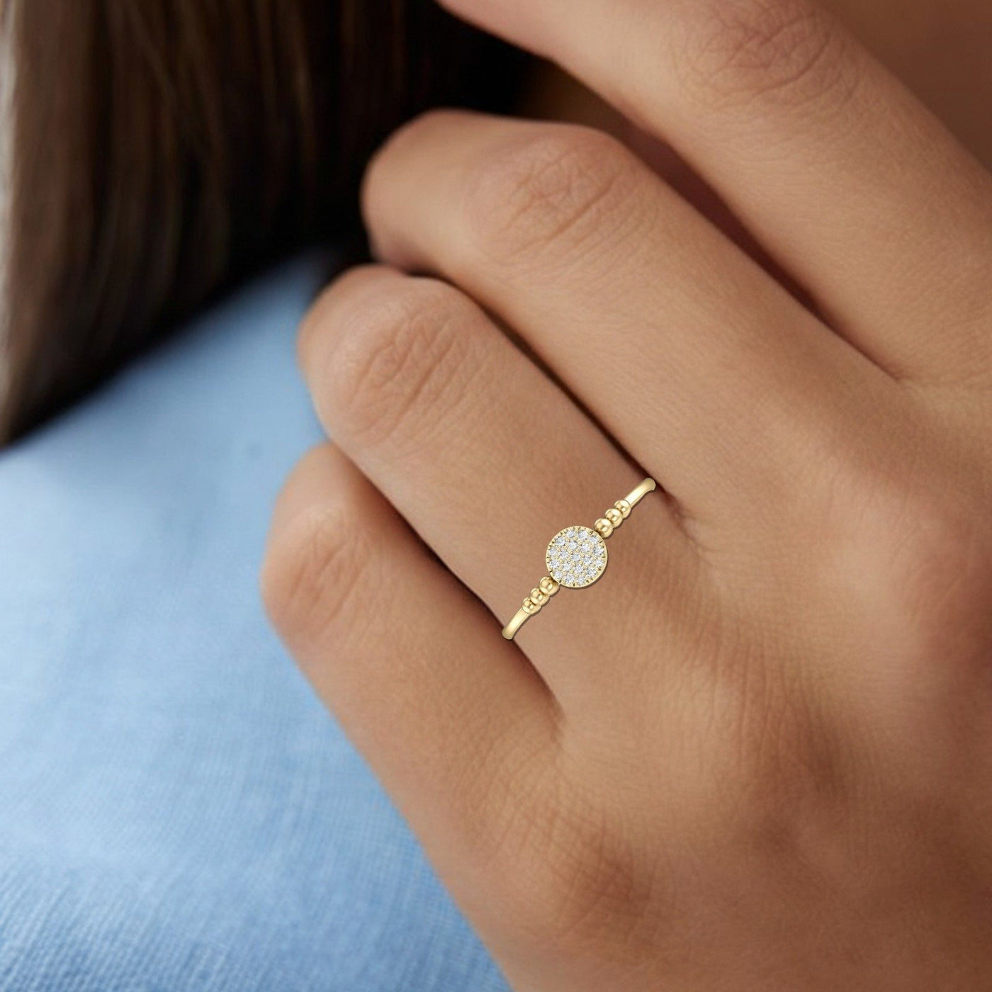 Gold ring with a diamond on a person's finger against a blue fabric background
