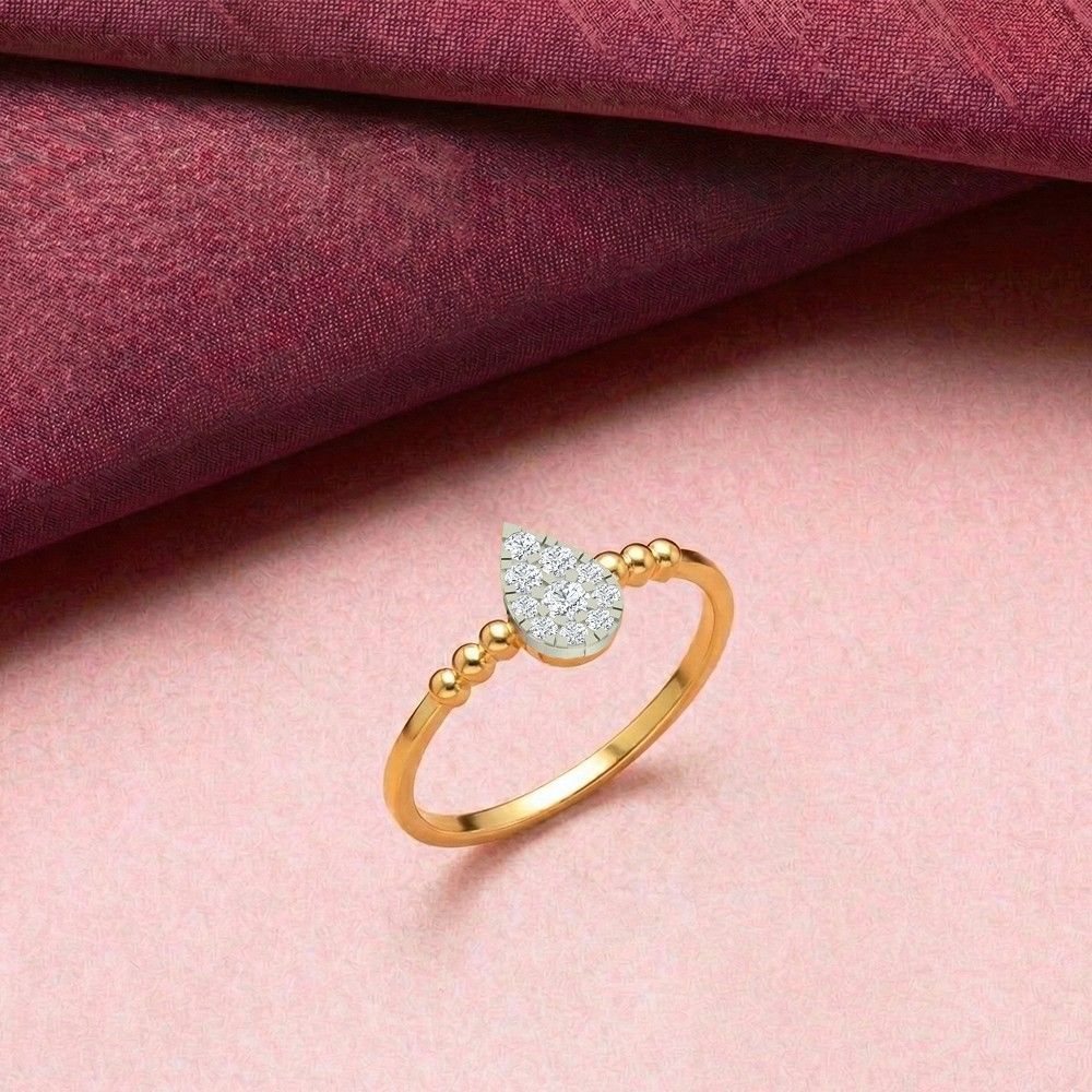 A gold ring featuring a teardrop-shaped diamond cluster in the center, set against a textured dark red background with a soft reflection below.