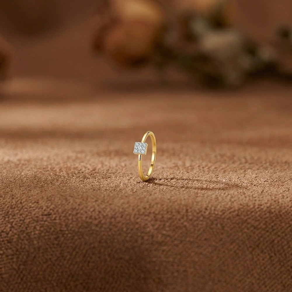 A delicate yellow gold ring with a square cluster ring,  on a textured brown fabric surface with a softly blurred background.