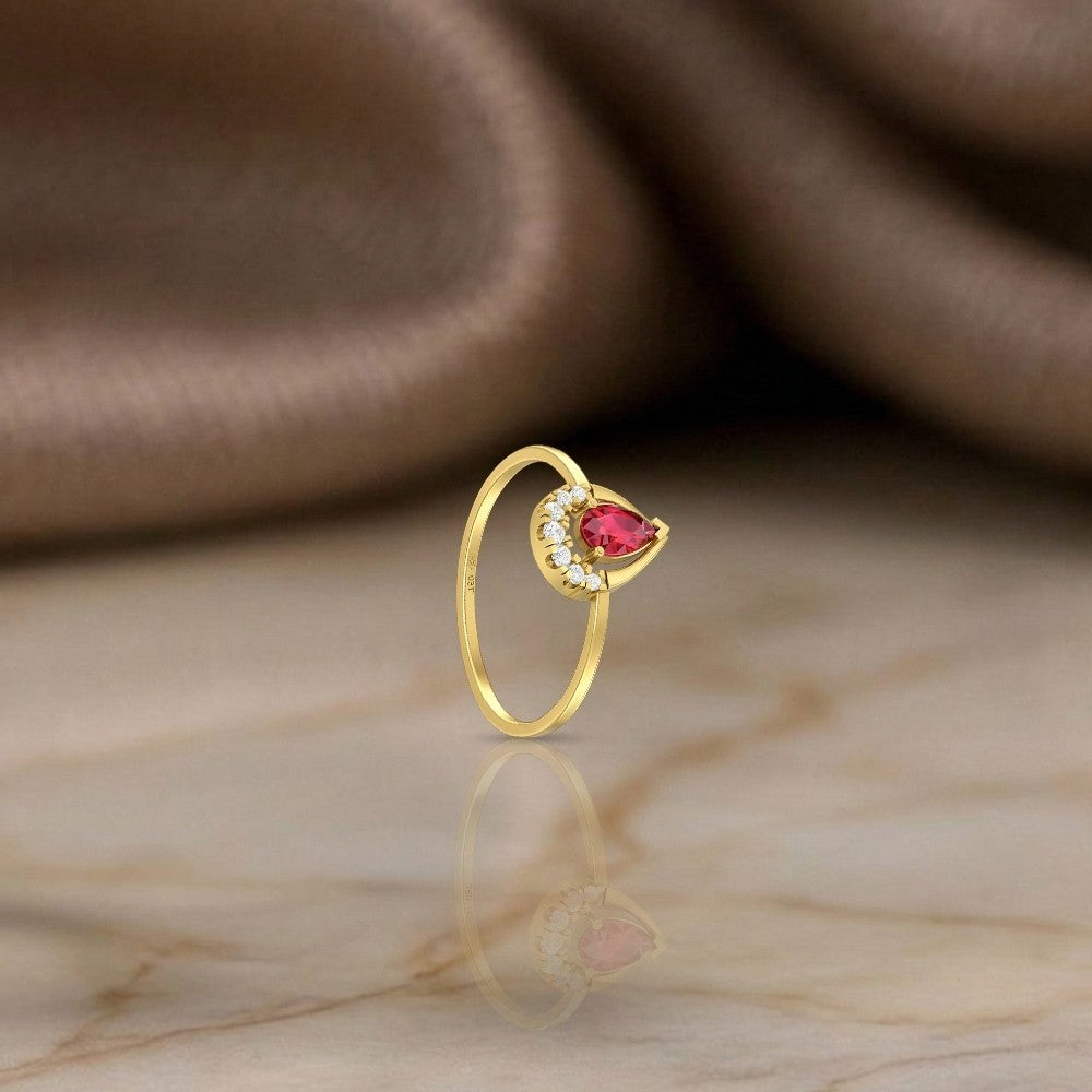 Gold and diamond with teardrop ruby gemstone on a reflective surface.