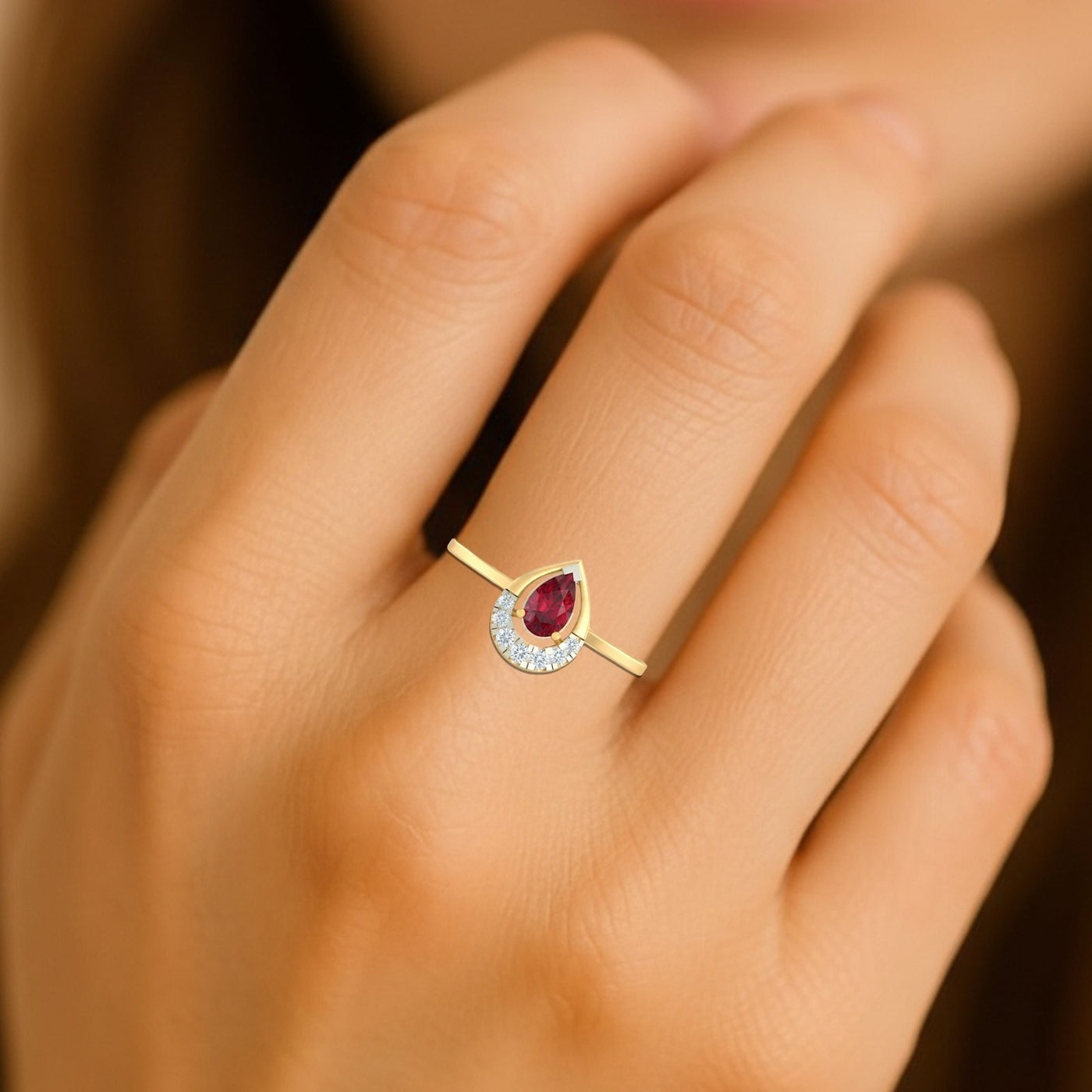 Gold and diamond with teardrop ruby gemstone on a person's finger.