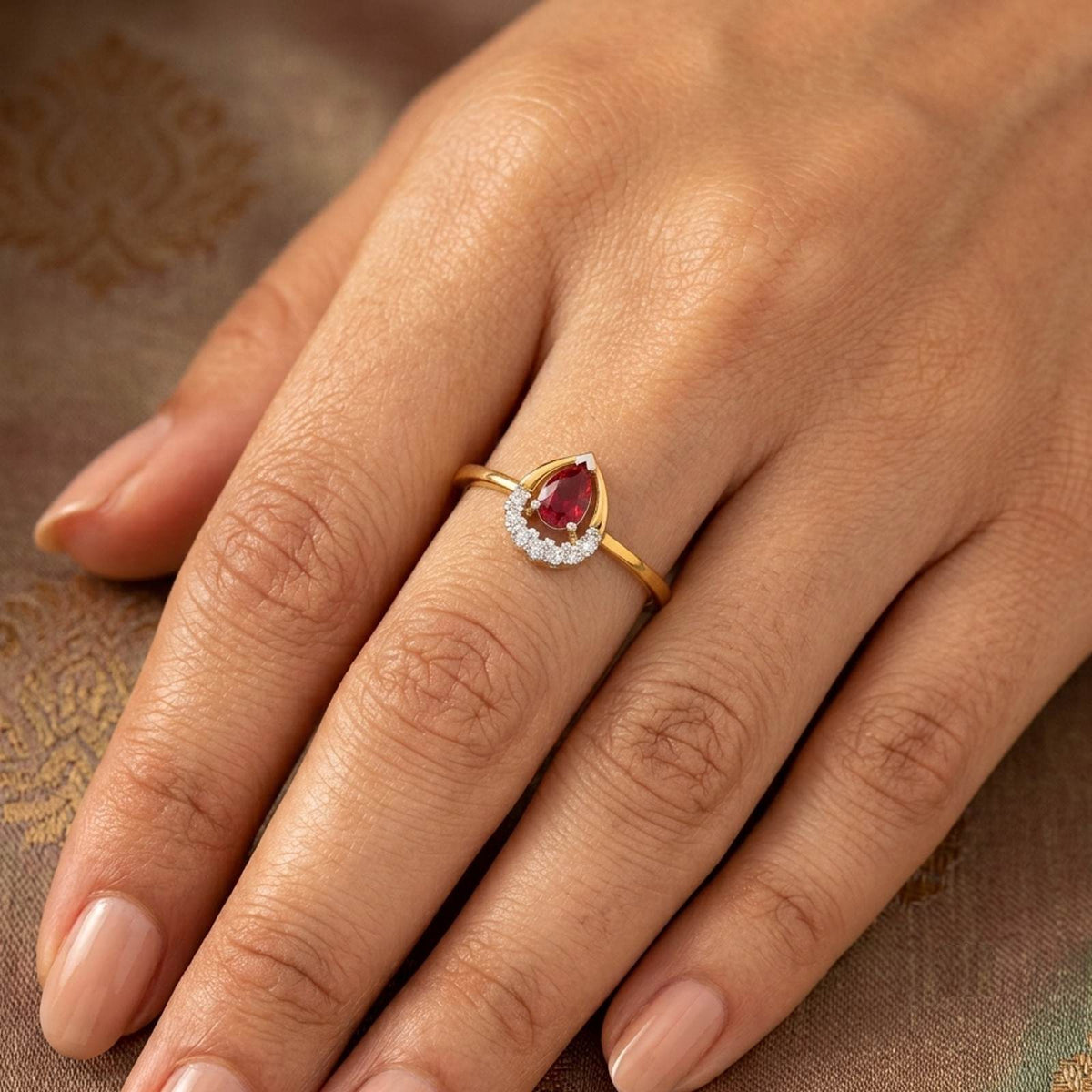 Gold and diamond with teardrop ruby gemstone on a person's finger.