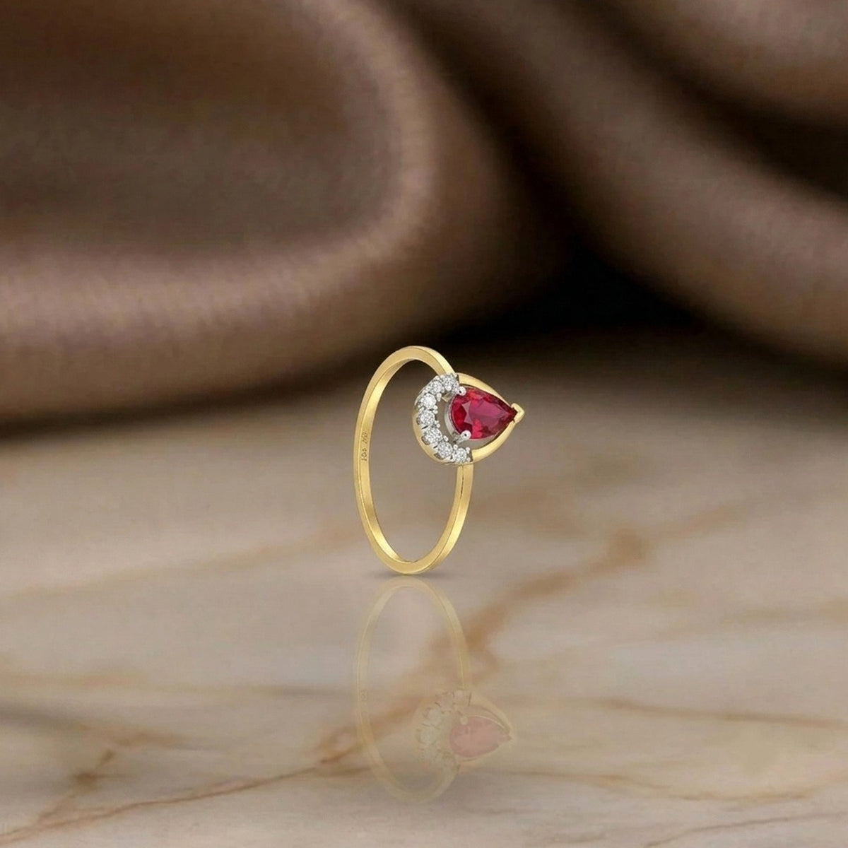 Gold and diamond with teardrop ruby gemstone on a reflective surface.