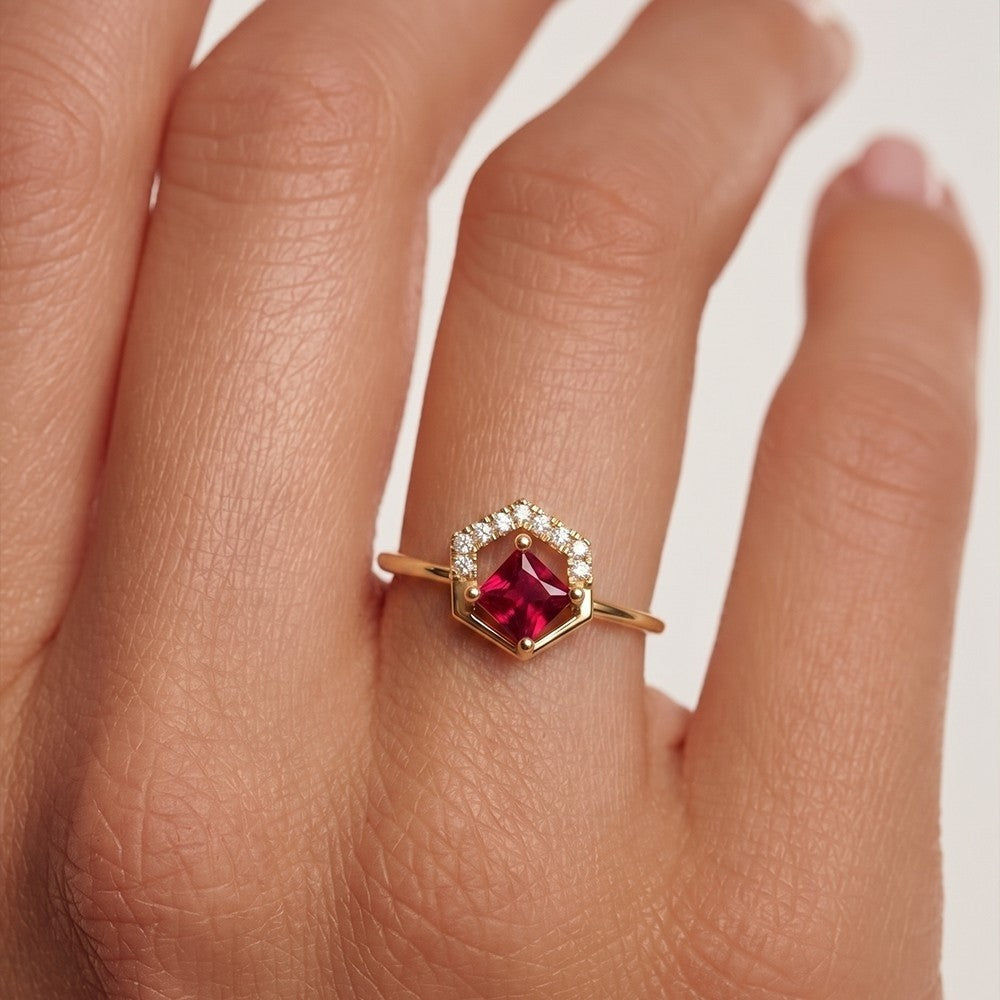 Gold ring with a ruby gemstone on a hand against a white background