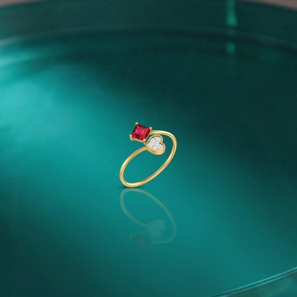Gold and diamond ring with a ruby gemstone on a reflective green surface