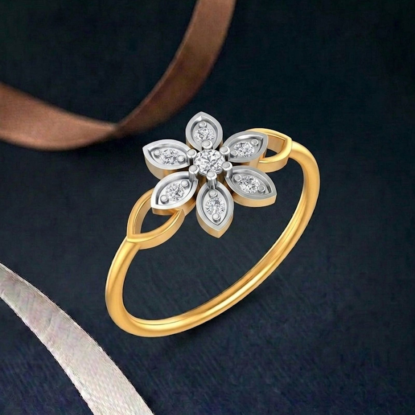 A gold ring featuring a flower-shaped setting with on a dark textured background with ribbon accents.