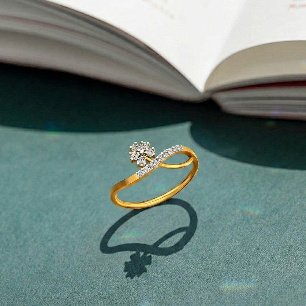 Gold ring with diamond floral design on a green surface with an open book in the background