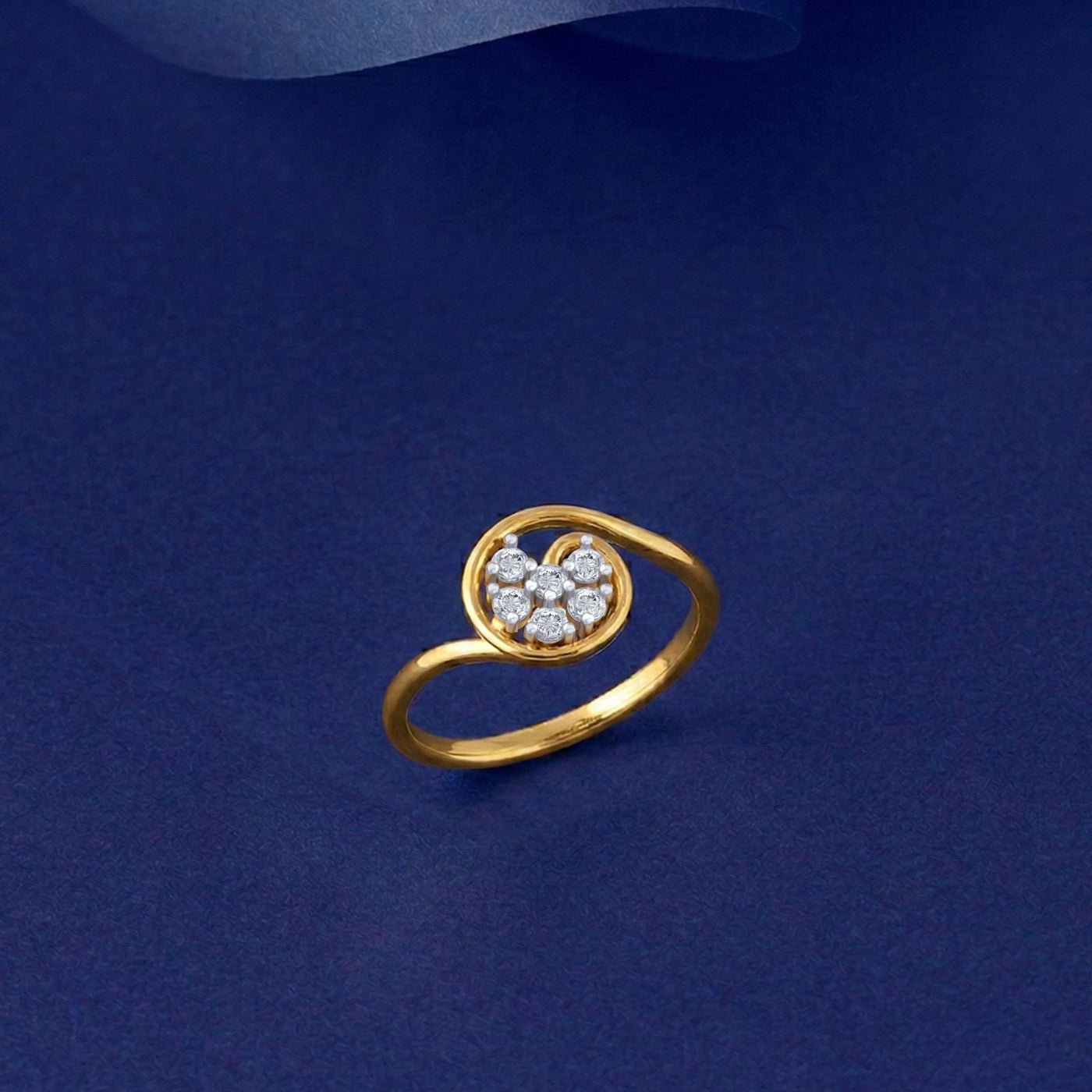 A gold ring featuring a circular flower motif, set on a dark blue textured background.