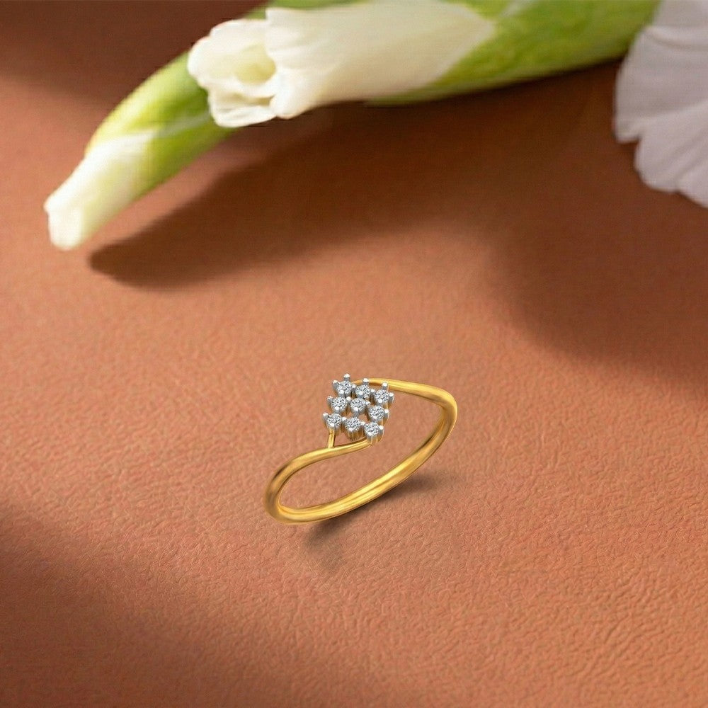 A gold ring with a small cluster on a warm brown textured surface, with blurred white flowers in the background.