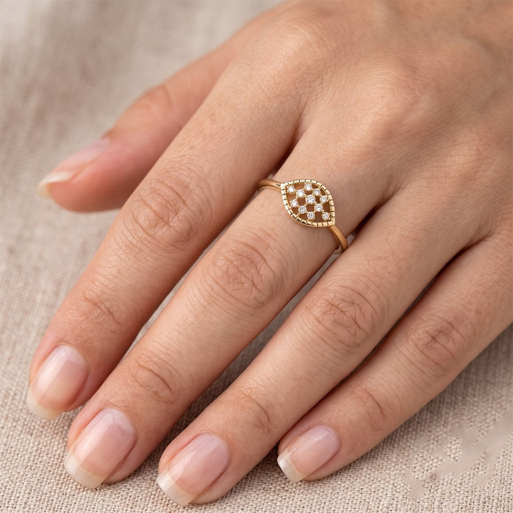 A close-up of a hand wearing a gold ring with a marquise-shaped on a textured beige fabric background.