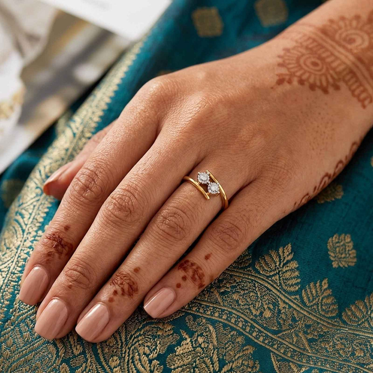 A close-up of a hand wearing a gold ring, resting on a teal and gold patterned fabric.