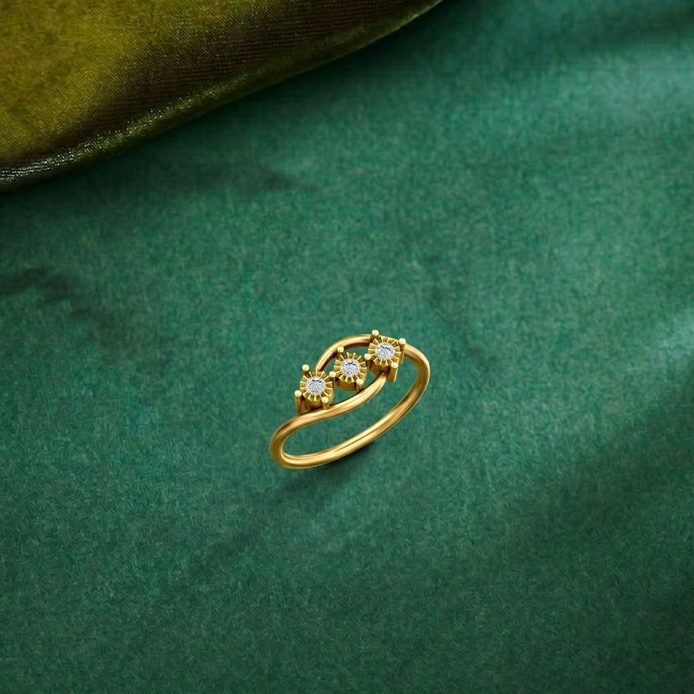 A gold ring with three small arranged in a floral or leaf-like cluster, resting on a textured dark green fabric surface.
