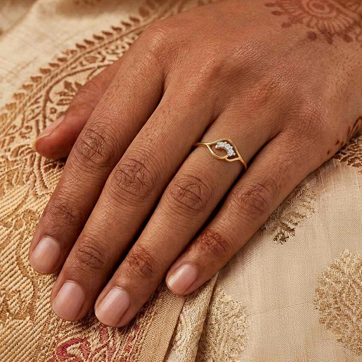 A close-up of a hand wearing a delicate gold ring, resting on a beige patterned fabric.