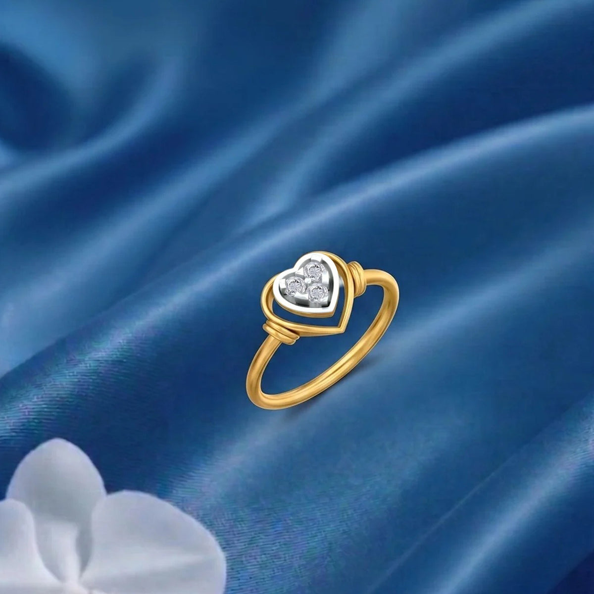Gold ring with a heart-shaped diamond setting on a blue fabric surface.